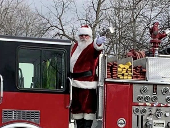 Santa Tom waving from a fire truck during a community Christmas parade.