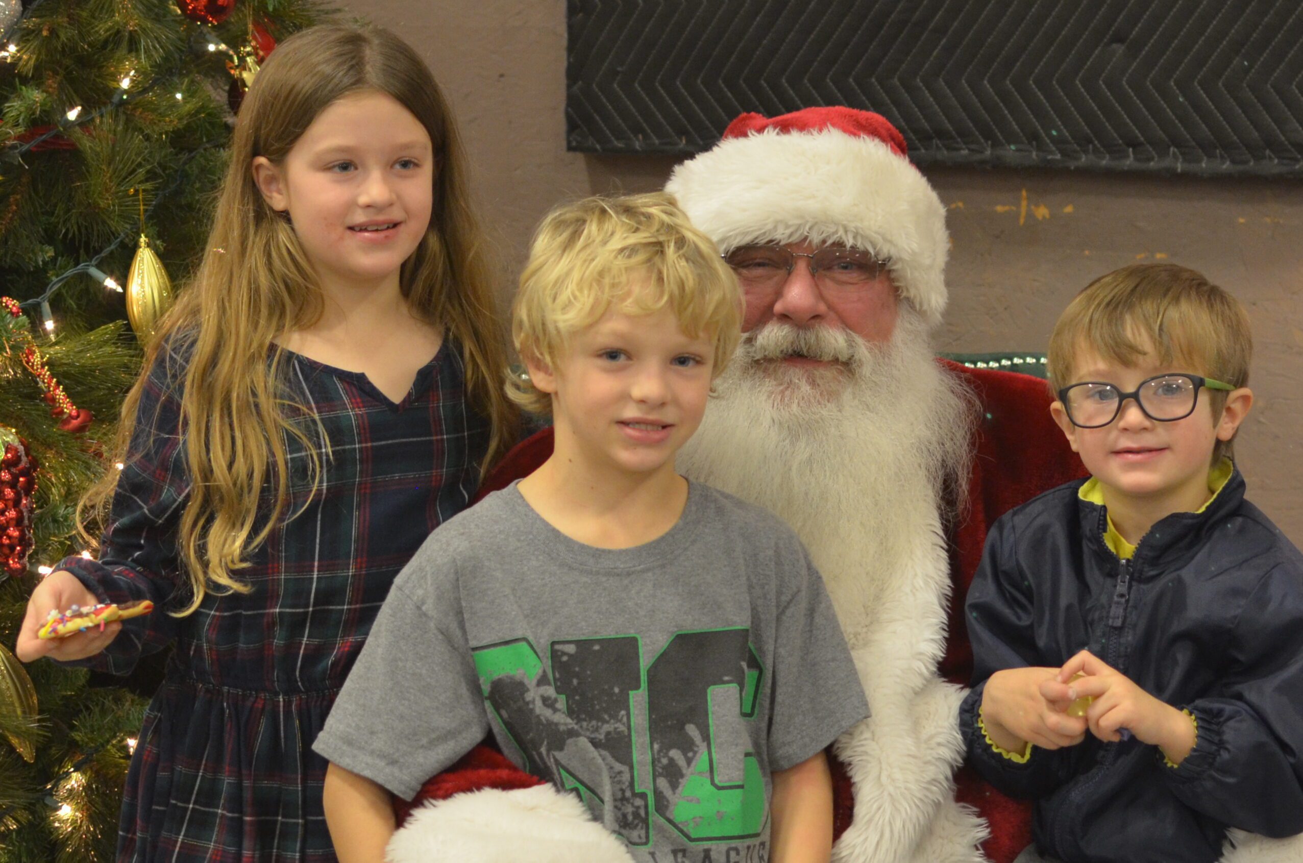 Santa Tom sitting with a group of siblings in front of a Christmas tree