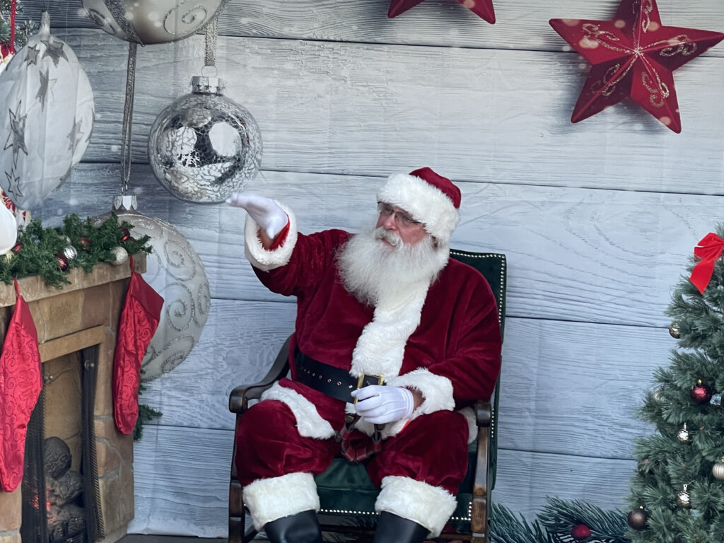 Santa Tom sitting next to a fireplace and greeting guests