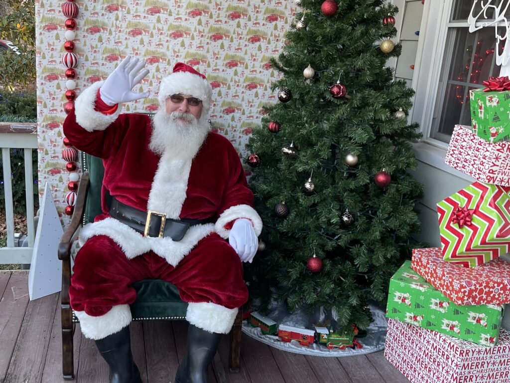 Santa Tom waving to guests from a festive Christmas porch display.