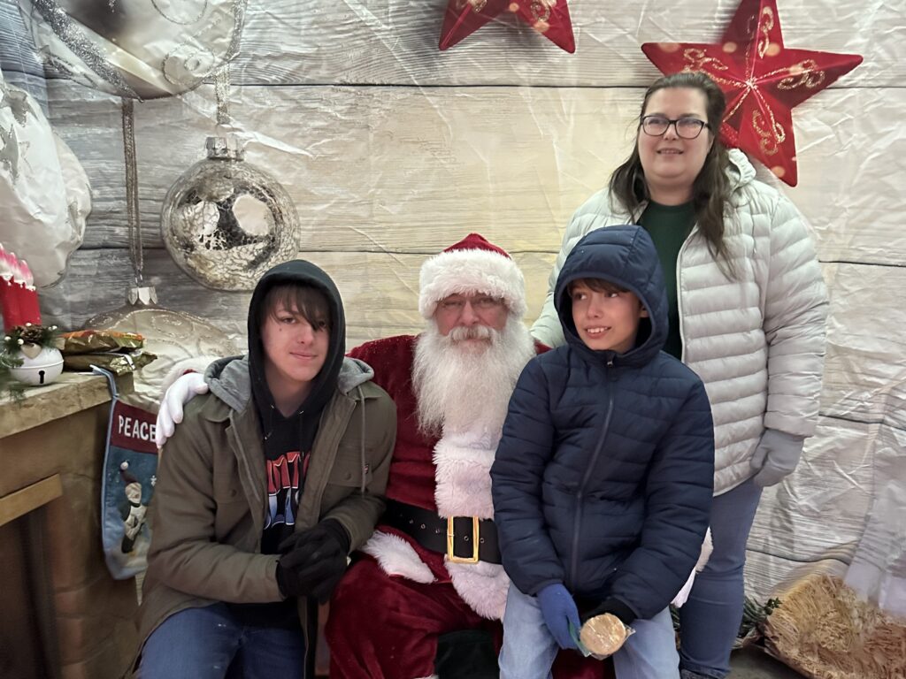 Family posing with Santa Tom during an outdoor Christmas celebration.