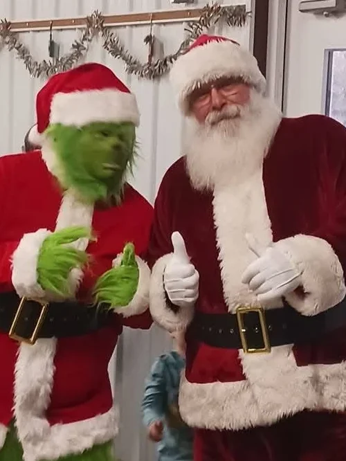 Santa Tom and the Grinch giving a thumbs up at a Christmas celebration
