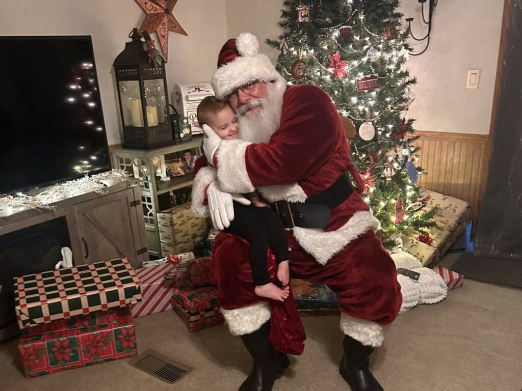 Santa Tom sharing a warm Christmas hug with a young child during a private visit.