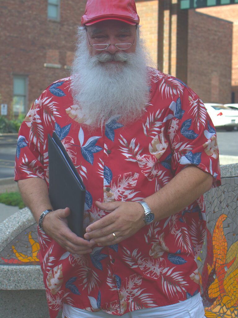 Santa Tom in a red Hawaiian shirt holding a folder and smiling during a Columbia, Missouri photo session.