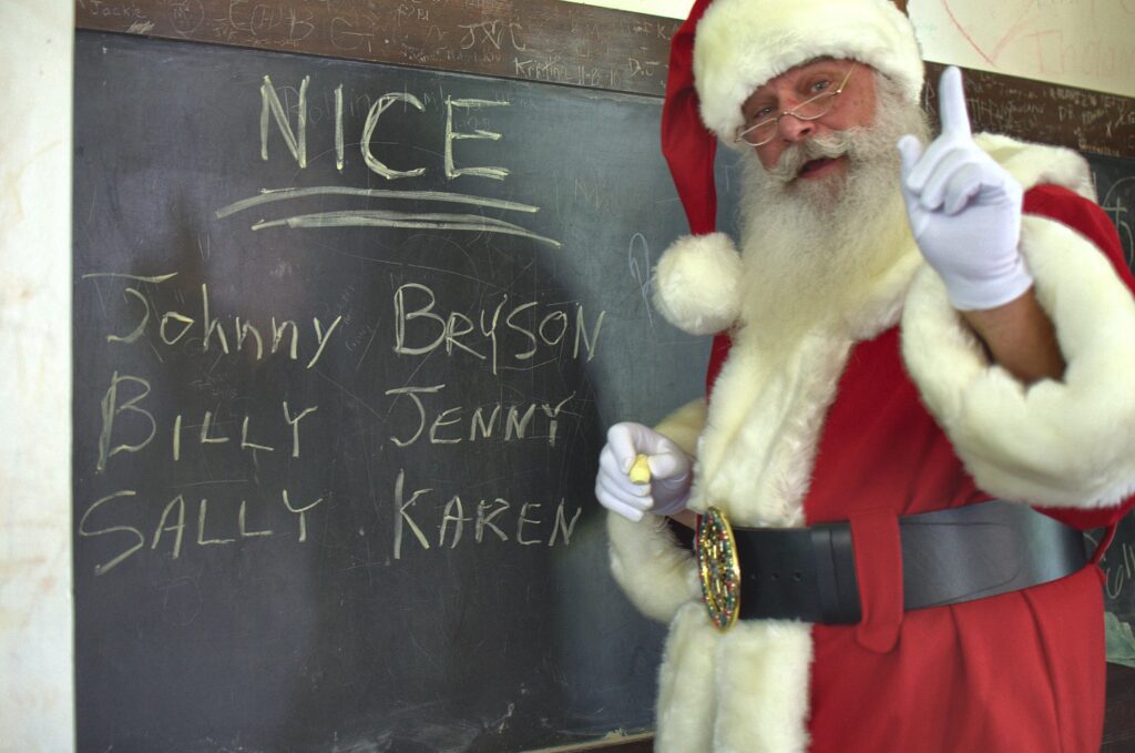 Santa Tom in a red Santa suit standing beside a chalkboard labeled Nice in Columbia, Missouri.