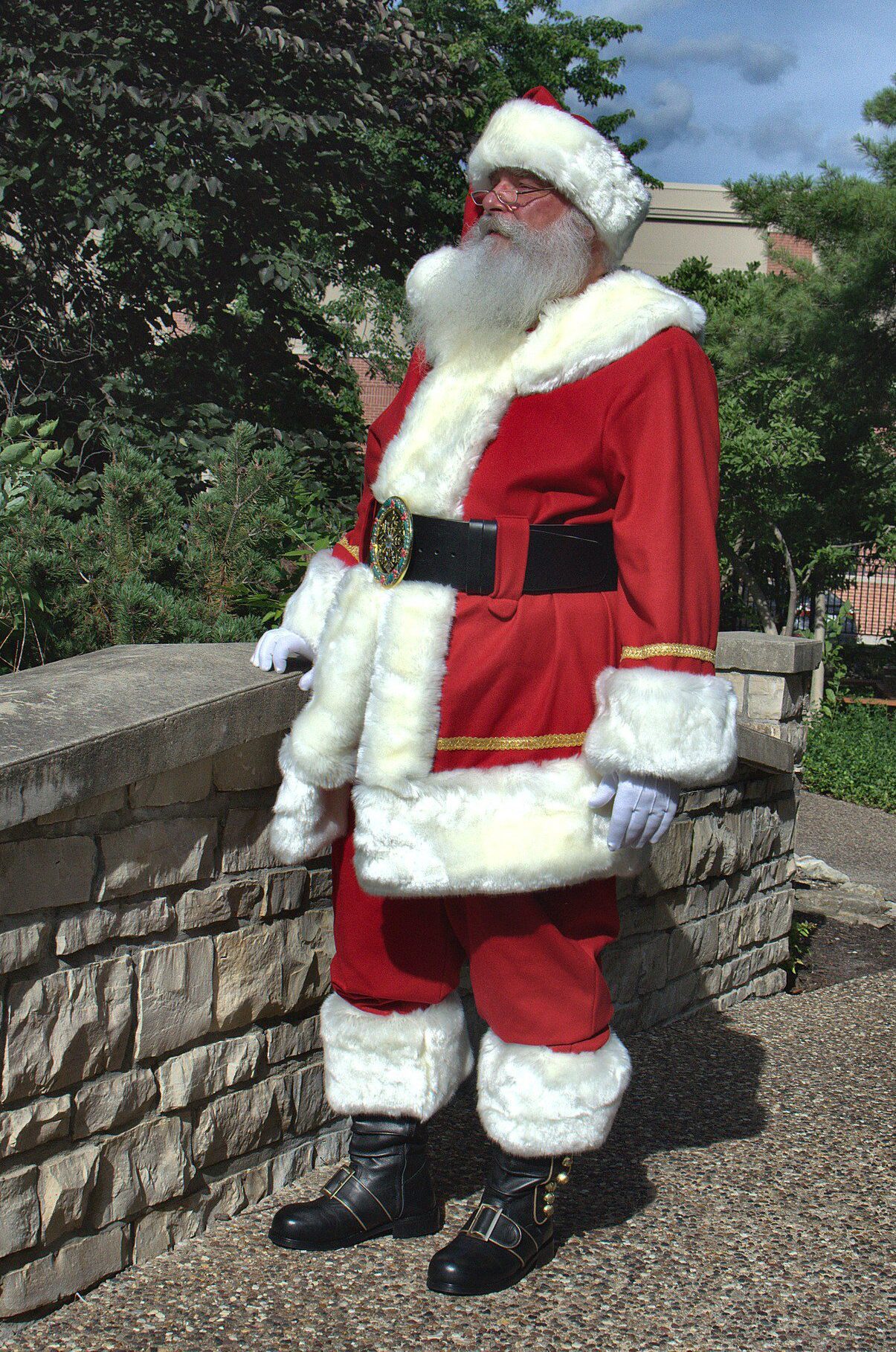 Santa Tom in a red Santa suit standing near a stone wall and greenery in Columbia, Missouri.