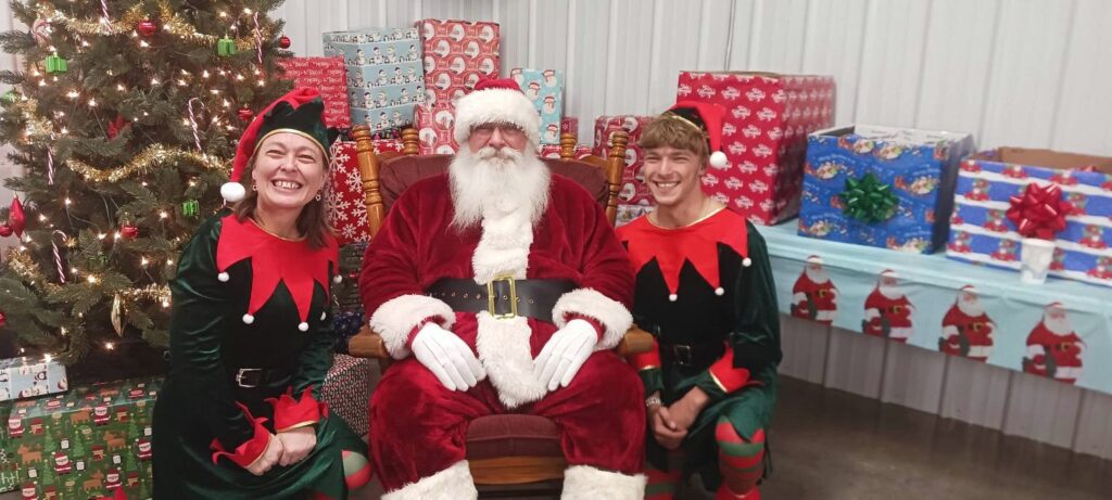 Santa Tom seated with Christmas event helpers at a community photo opportunity