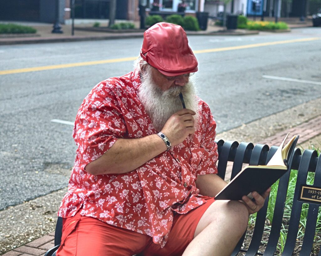 Santa Tom sitting on a downtown Jefferson City bench while reviewing a book for upcoming Santa visits.