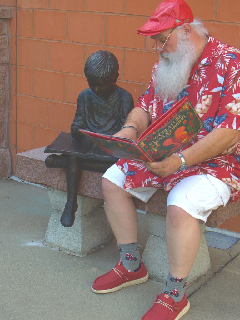 Santa Tom sits beside a child sculpture and points to an open picture book in Columbia, Missouri.