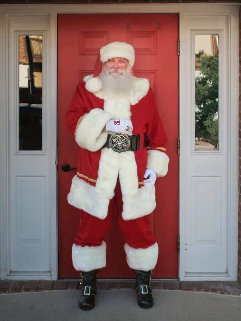 Santa Tom standing in his full red suit in a red doorway.