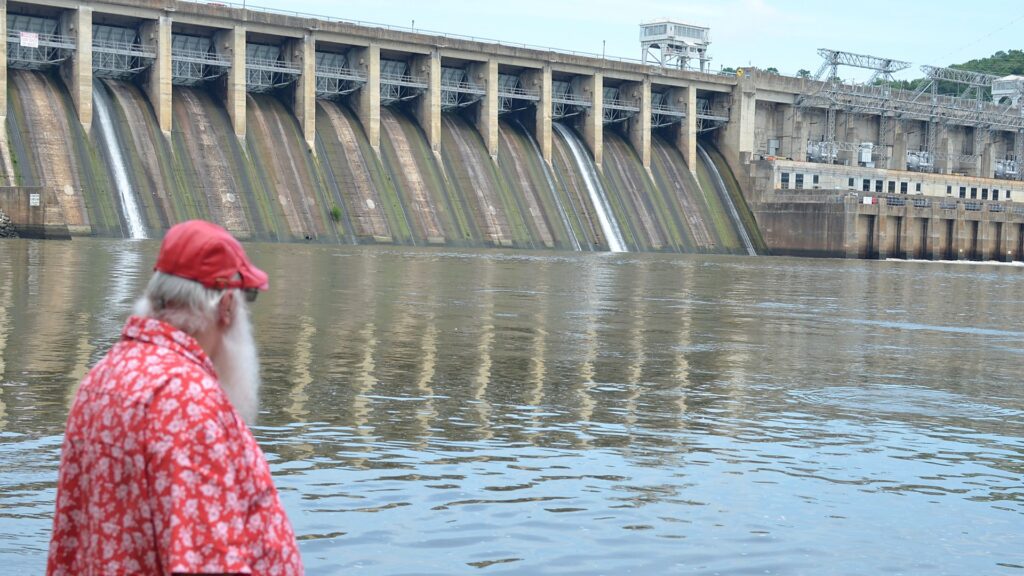 Santa Tom standing near lake water and a dam in the Lake of the Ozarks area.